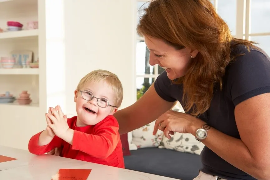 A woman and a smiling young boy at a table together during a therapy session at home